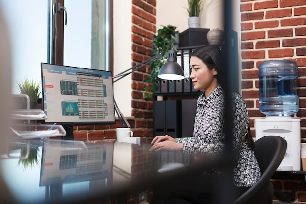 Young confident business woman reviewing startup project status charts while sitting in modern office. Marketing research company office worker analyzing organization financial statistics and data.