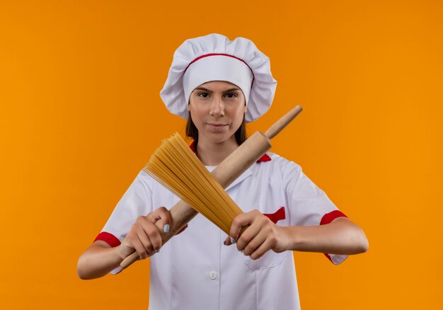 요리사 유니폼에 젊은 자신감 백인 요리사 소녀 롤링 핀과 복사 공간 오렌지 공간에 고립 된 스파게티의 무리 십자가