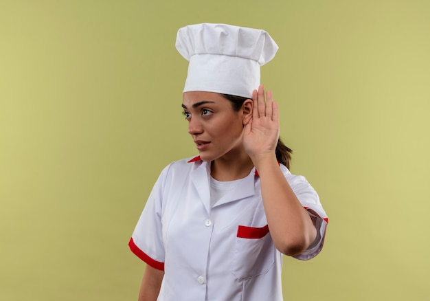 Молодая уверенная в себе кавказская девушка-повар в жестах шеф-повара не слышит знак на зеленой стене с копией пространства