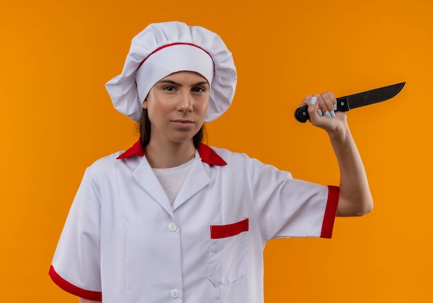 Free photo young confident caucasian cook girl in chef uniform holds knife on orange  with copy space