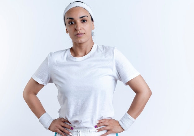 Free photo young confident caucasian sporty woman wearing headband and wristbands puts hands on waist isolated on white space with copy space