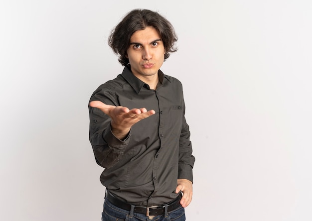 Young confident handsome caucasian man holds hand out and looks at camera isolated on white background with copy space