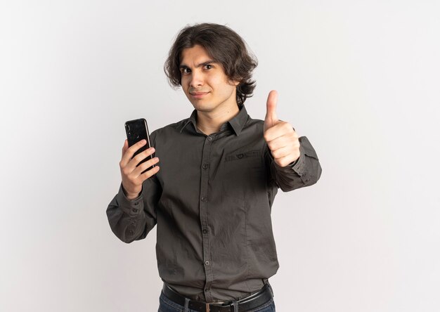 Young confident handsome caucasian man holds phone and thumbs up isolated on white background with copy space