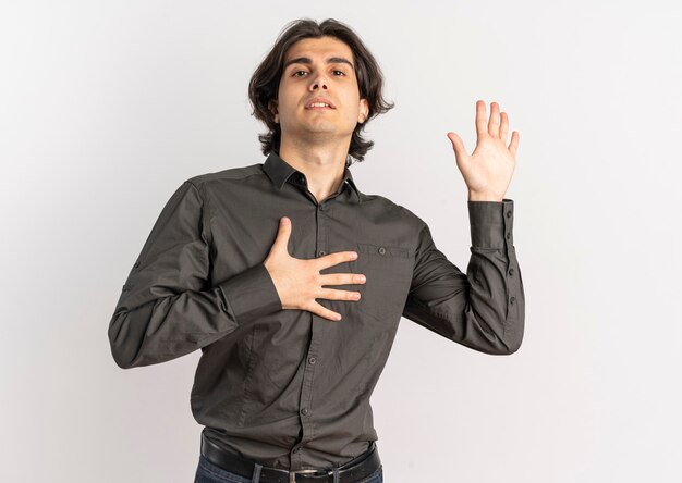 Молодой уверенный в себе красивый кавказский мужчина кладет руку на грудь и поднимает руку вверх, изолированную на белом фоне с копией пространства