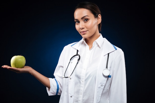 Young confident lady doctor holding apple and looking