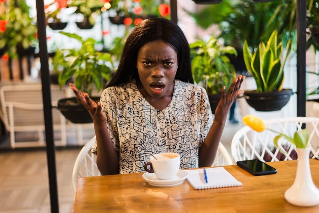 コーヒーショップでショックを受けた若い混乱したアフリカの女性