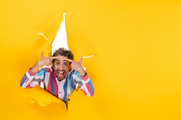 Young confused bearded guy in a torn hole and free space in yellow paper