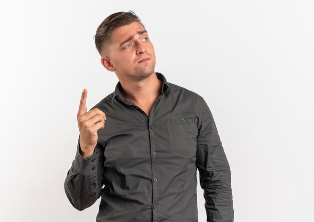Young confused blonde handsome man points up looking at side isolated on white background with copy space
