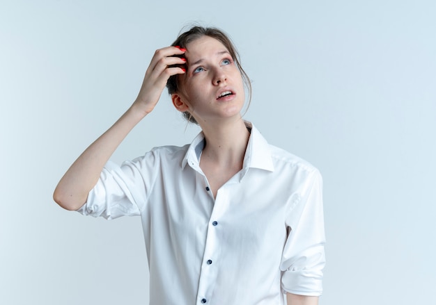 Young confused blonde russian girl puts hand on forehead looking up isolated on white space with copy space