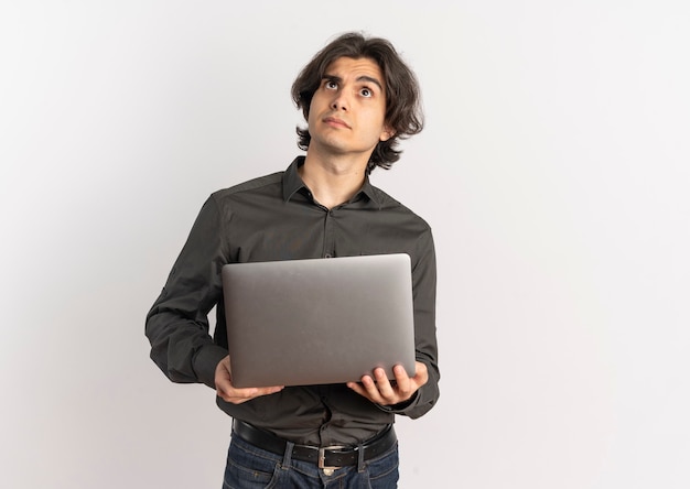 Young confused handsome caucasian man holds laptop and looks up isolated on white background with copy space