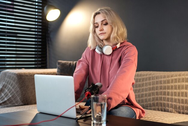 Young content creator blonde girl with headphones working on her laptop on the table with camera