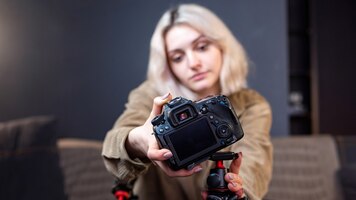 Бесплатное фото Молодой создатель контента блондинка улыбается девушка, ставя камеру на штатив. работать из дома. начинаем снимать видеоблог