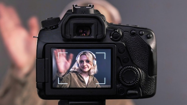 Young content creator blonde talking and gesturing girl filming herself using a camera on a tripod