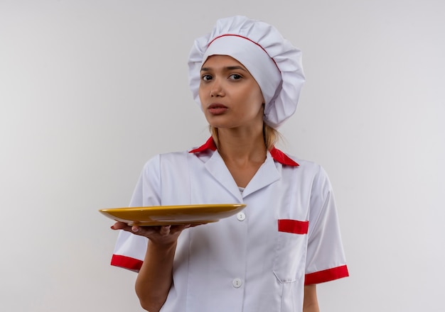  young cook female wearing chef uniform holding plate on isolated white wall with copy space
