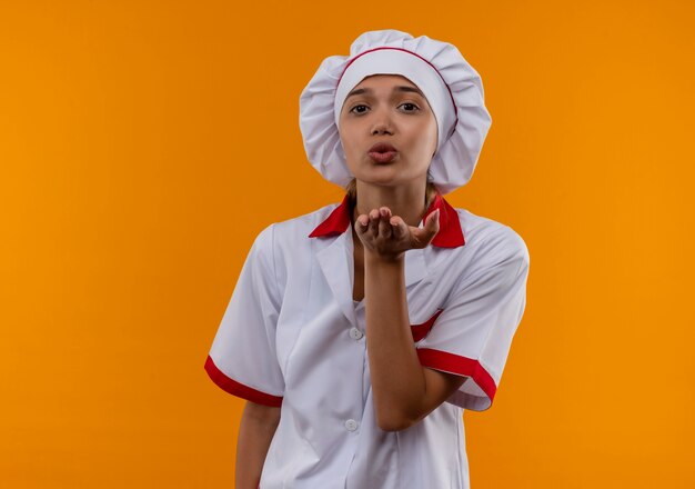  young cook female wearing chef uniform showing kiss gesture on isolated orange wall with copy space