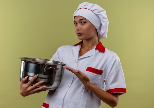  young cook female wearing chef uniform showing saucepan in her hand on isolated green wall