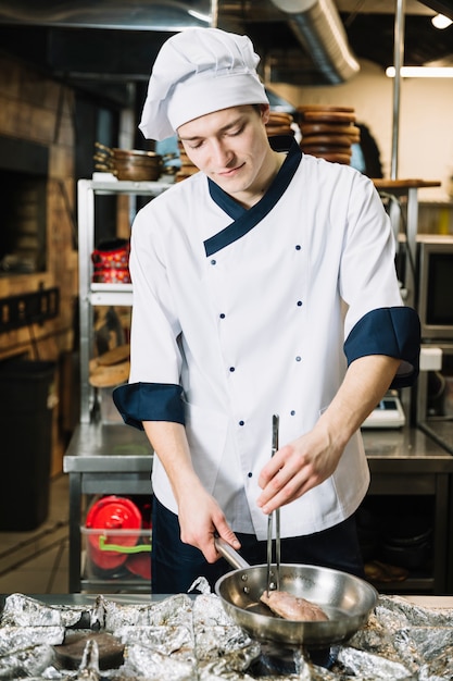 Young cook frying meat in pan on stove