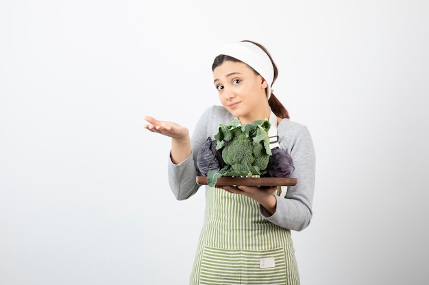 Young cook holding plate of cabbage and broccoli and showing open space