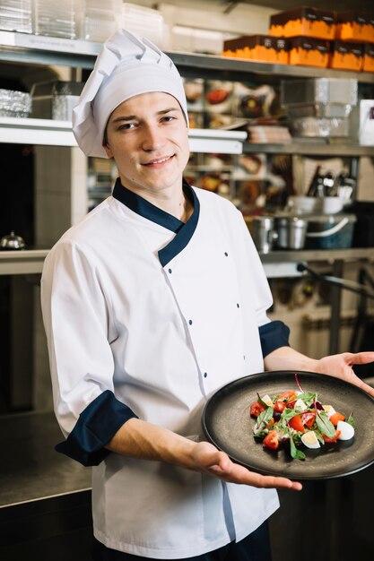 Young cook holding plate with vegetarian salad