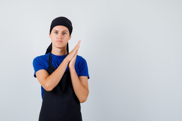 Young cook man rubbing palms in t-shirt, apron and looking serious. front view.