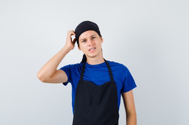 Young cook man scratching head in t-shirt, apron and looking pensive. front view.