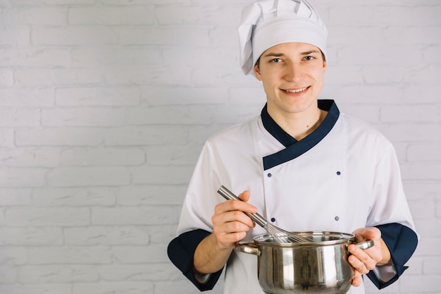 Young cook whipping something in small pot with whisk