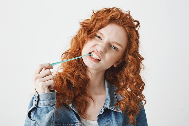 Free photo young cool brutal redhead girl in jean jacket chewing gum over white background.