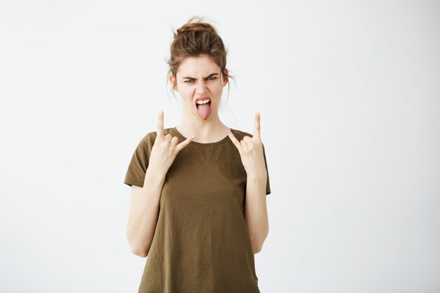 Young cool woman with bun showing tongue and rock sign.