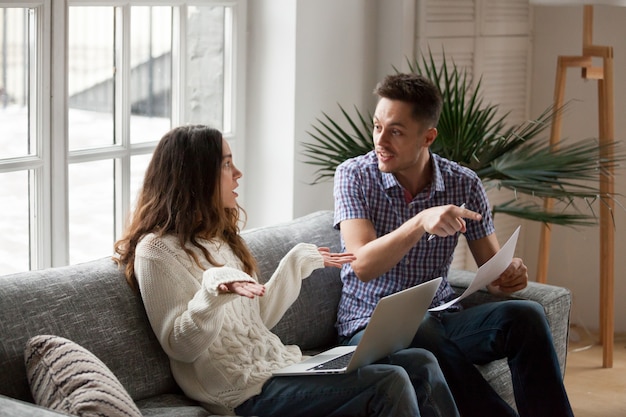 Young couple arguing about high bills with laptop and documents