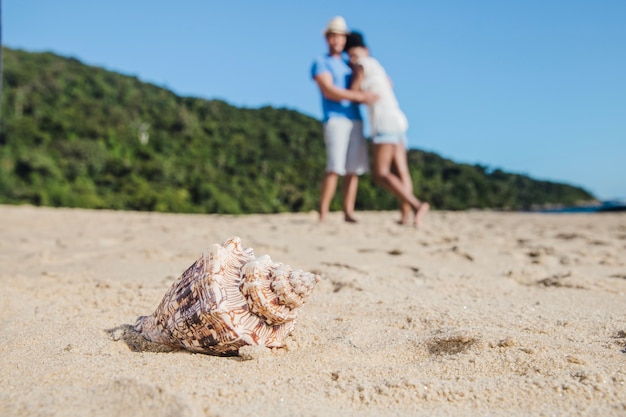 Young couple at the beach with seashell in foreground