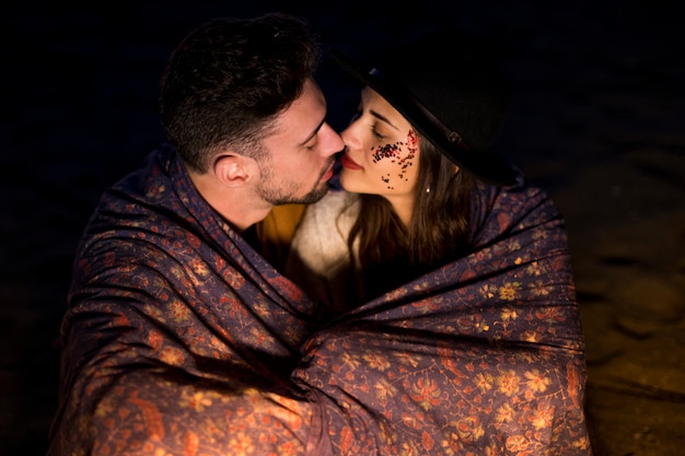 Young couple in blanket sitting on sandy sea shore