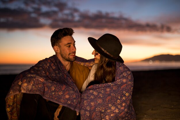 Young couple in blanket smiling on sea shore