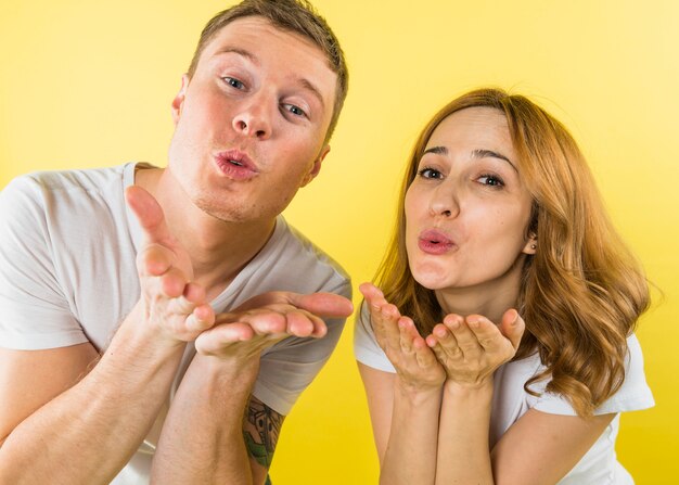 Young couple blowing kisses in front of camera against yellow backdrop
