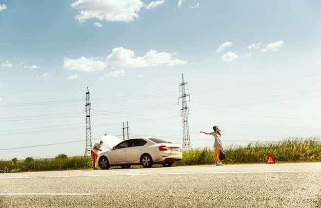 若いカップルは休憩の途中で車を壊した。彼らは他のドライバーを止めて助けやヒッチハイクを求めようとしています。関係、道路上のトラブル、休暇。