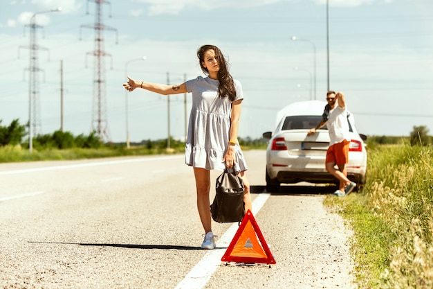 若いカップルは休憩の途中で車を壊した。彼らは他のドライバーを止めて助けやヒッチハイクを求めようとしています。関係、道路上のトラブル、休暇。