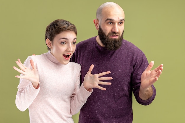 young couple in casual clothes bearded man and woman with short hair looking aside happy and surprised valentines day concept standing over green wall