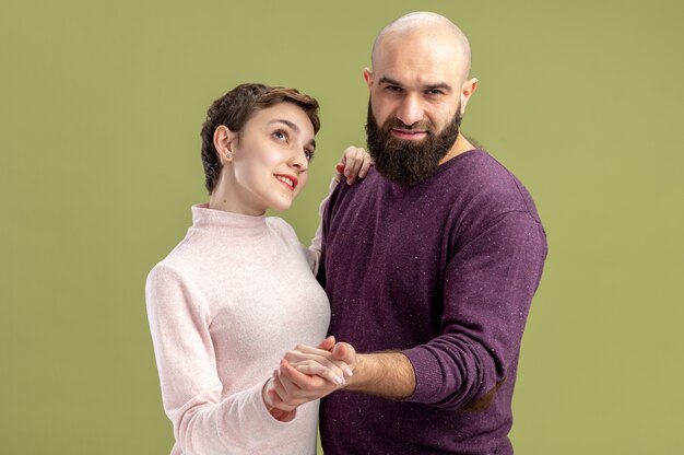 young couple in casual clothes happy bearded man and woman with short hair happy in love together dancing celebrating valentines day standing over green wall