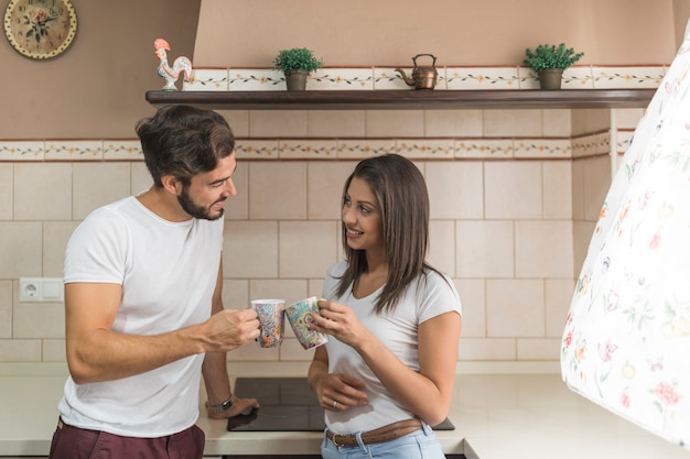 Free photo young couple clinking mugs in kitchen