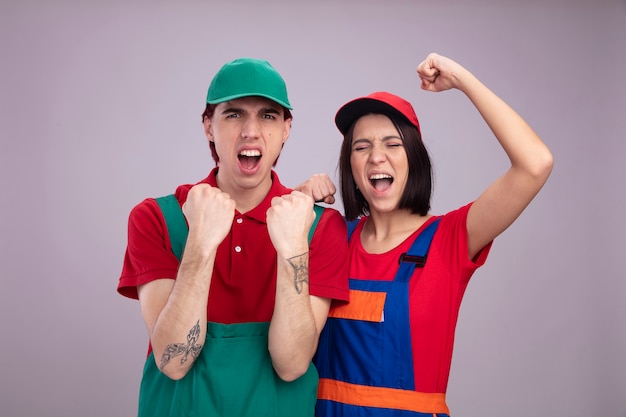 Young couple in construction worker uniform and cap doing yes gesture guy girl with closed eyes 