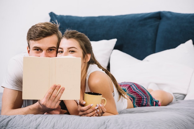 無料写真 ベッドの上の本で顔を覆っている若いカップル