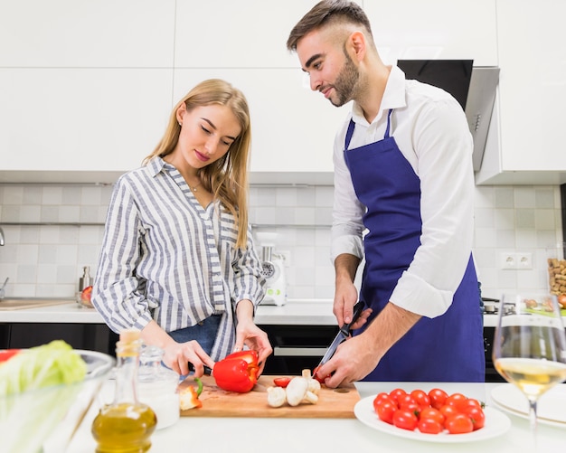 Young couple cutting vegetables for salad on board
