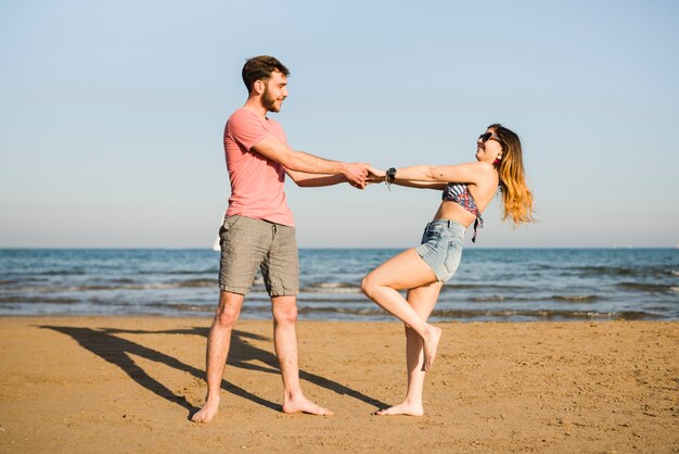 Молодая пара танцует на берегу моря на пляже против голубого неба
