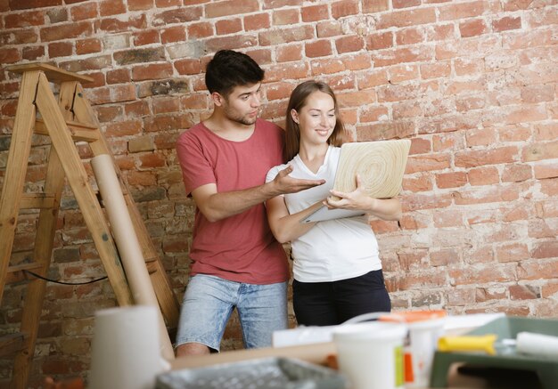 一緒にアパートの修理をしている若いカップル。家のイメージチェンジやリフォームをしている既婚男性と女性。関係、家族、愛の概念。ノートブックで壁のデザインを選択します。