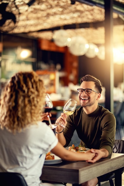 Бесплатное фото Молодая пара пьет вино и веселится во время обеда в баре в центре внимания мужчина