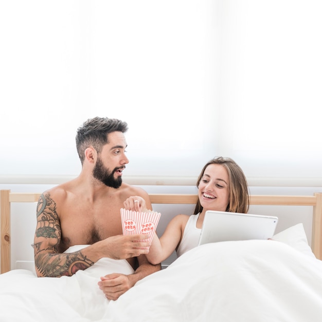 Free photo young couple eating popcorn on bed