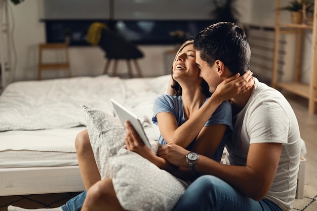 Young couple embracing and having fun while surfing the net on digital tablet in bedroom