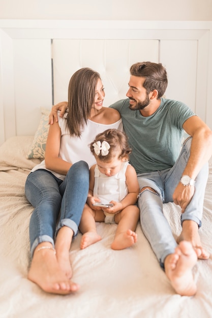 Young couple embracing near daughter with smartphone