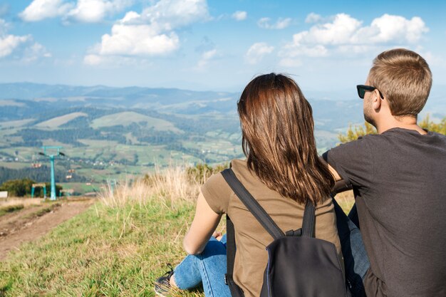 山の風景を楽しんで、丘の上に座っている若いカップル