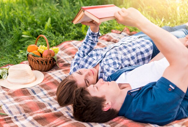 Young couple enjoying reading book on blanket