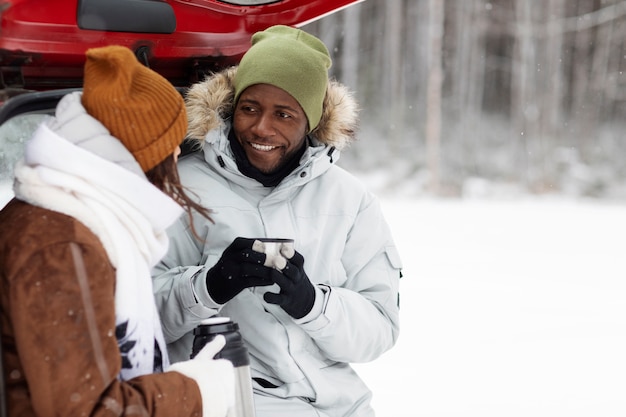 Young couple enjoying warm drinks during a winter road trip in the car's trunk